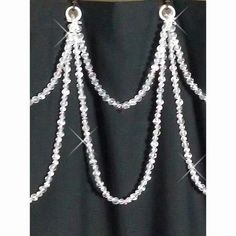 a black curtain with some white beads hanging from it's side and two silver chains attached to it