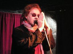 a man standing in front of a microphone with his hands up to his face while wearing sunglasses