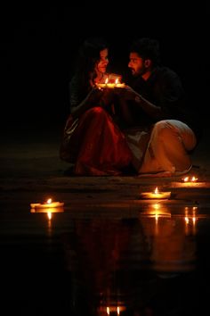 two people sitting on the ground holding candles