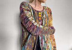 a woman standing against a wall wearing a colorful cardigan sweater with buttons on it