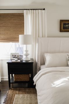 a bed with white linens and pillows in a bedroom next to a lamp on a night stand