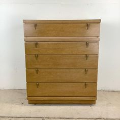 a wooden dresser sitting on top of a floor next to a white wall with metal handles