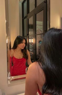 a woman in a red dress looking at herself in the mirror with long black hair