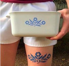 a person holding a white bowl with blue flowers on it's side and the bottom part of their leg