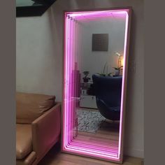 a pink lighted mirror sitting on top of a wooden floor next to a brown couch