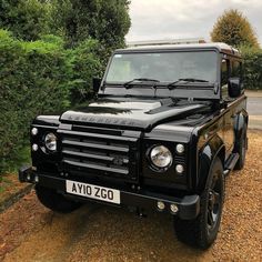 a black land rover is parked in front of some bushes