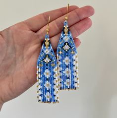 a pair of blue and white beaded earrings in the palm of someone's hand