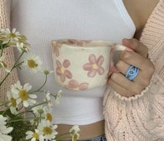 a woman holding a coffee cup with daisies in front of her and a bouquet of flowers behind her