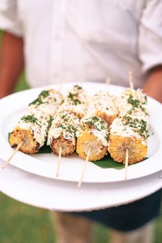 a person holding a white plate with food on it and toothpicks in the middle