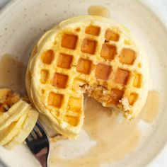 a waffle on a plate with syrup and a fork in the bowl next to it