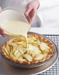 a person pouring milk into a pie on top of a metal pan covered in apples