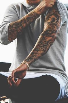 a man with tattoos on his arm sitting down and holding his hand near his face