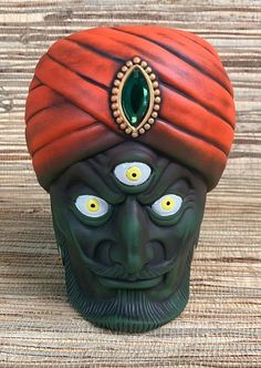 a green man's head with yellow eyes and a red turban on top