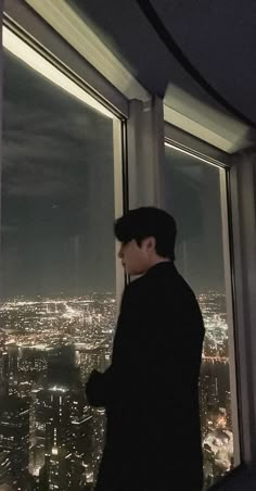 a man standing in front of a window looking out at the city lights and skyscrapers