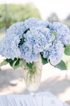 a vase filled with blue flowers sitting on top of a table next to napkins