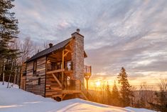 a log cabin sits on top of a snow covered hill with the sun setting in the background