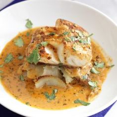 a white plate topped with fish covered in sauce and garnished with green leaves