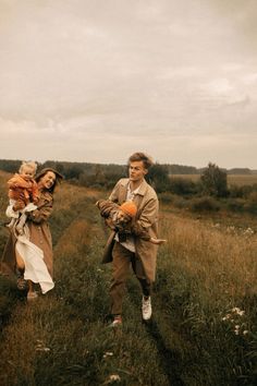 a man and woman walking through a field with two children on their shoulders, one holding an orange ball