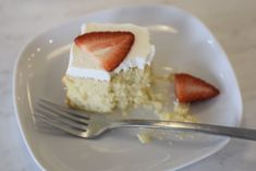 a piece of cake with white frosting and strawberries on top is sitting on a plate next to a fork