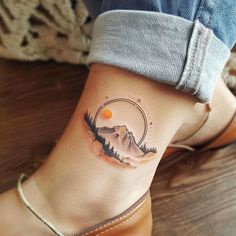 a woman's foot with a mountain and sun tattoo on the side of her ankle