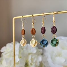 four different colored cups are hanging from gold earwires on a stand with white flowers in the background