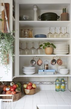 an open kitchen cupboard filled with lots of dishes and fruit on top of white counter tops