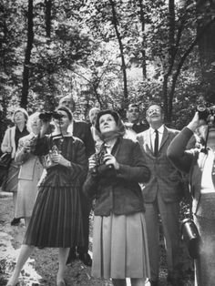 an old black and white photo of people standing in the woods with their hands up