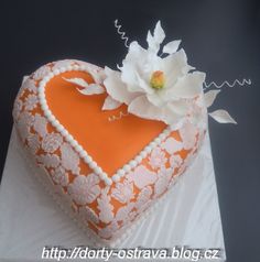 an orange and white heart shaped cake with flowers on the top is sitting on a table