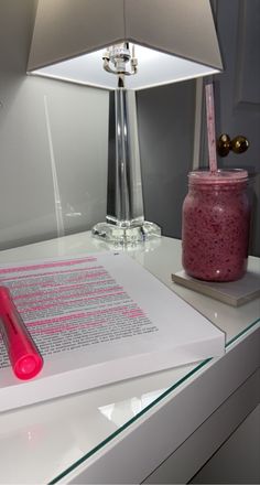 a pink pen sitting on top of a white desk next to a lamp and paper