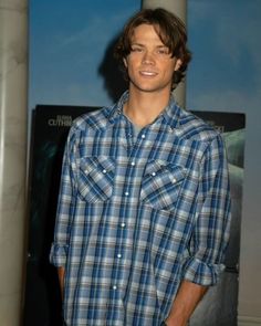 a man standing in front of a movie poster wearing a blue and white plaid shirt