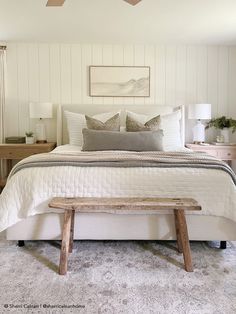 a bedroom with a white bed, wooden bench and ceiling fan in the middle of it