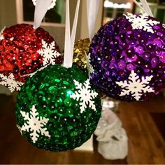 three christmas ornaments hanging from strings with snowflakes on them, one is green and the other is red