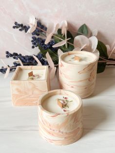 three candles sitting next to each other on a white table with flowers in the background