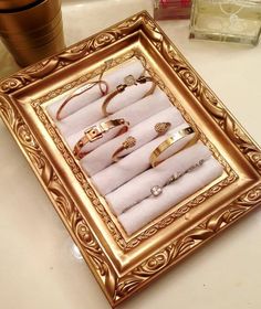 there are many different types of rings in a gold frame on the table next to a cup