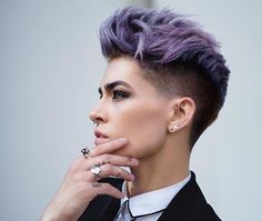 a woman with purple hair and piercings on her ear looking off to the side