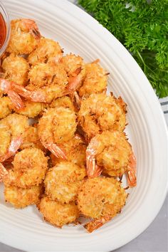 fried shrimp with dipping sauce on a white platter next to parsley and tomatoes