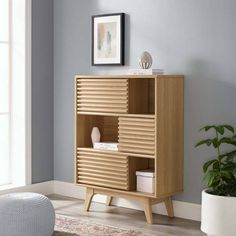 a wooden shelf with drawers in a living room next to a potted plant on the floor