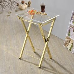 a glass table with gold legs on the floor next to a magazine rack and pictures