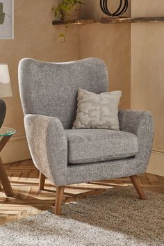 a gray chair sitting on top of a wooden floor next to a table with a lamp