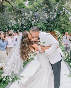 a bride and groom kiss as bubbles fly in the air above them at their wedding