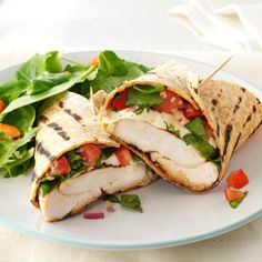 a white plate topped with a cut in half sandwich next to lettuce and tomatoes