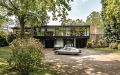 a car is parked in front of a large house with trees and bushes around it