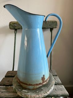 an old blue pitcher sitting on top of a wooden table next to a chair and wall