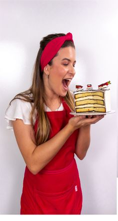 a woman in an apron holding a cake and making a funny face with her mouth wide open