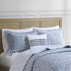 a bed with blue and white comforters on top of it next to a wooden headboard