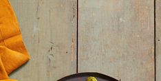 a black plate topped with green vegetables on top of a wooden table next to a yellow napkin