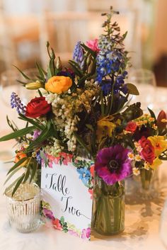 a vase filled with lots of colorful flowers on top of a white table cloth covered table