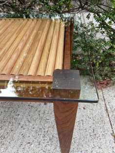 a wooden bench sitting on top of a cement ground next to a tree and shrubbery