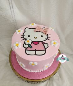 a pink hello kitty cake with white flowers on the top and bottom, sitting on a table