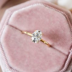 an engagement ring sits on top of a pink velvet box with a diamond in it